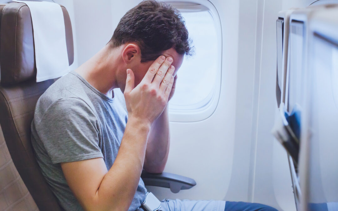 Male passenger has a headache on an airplane, feeling bad, with head in hands.